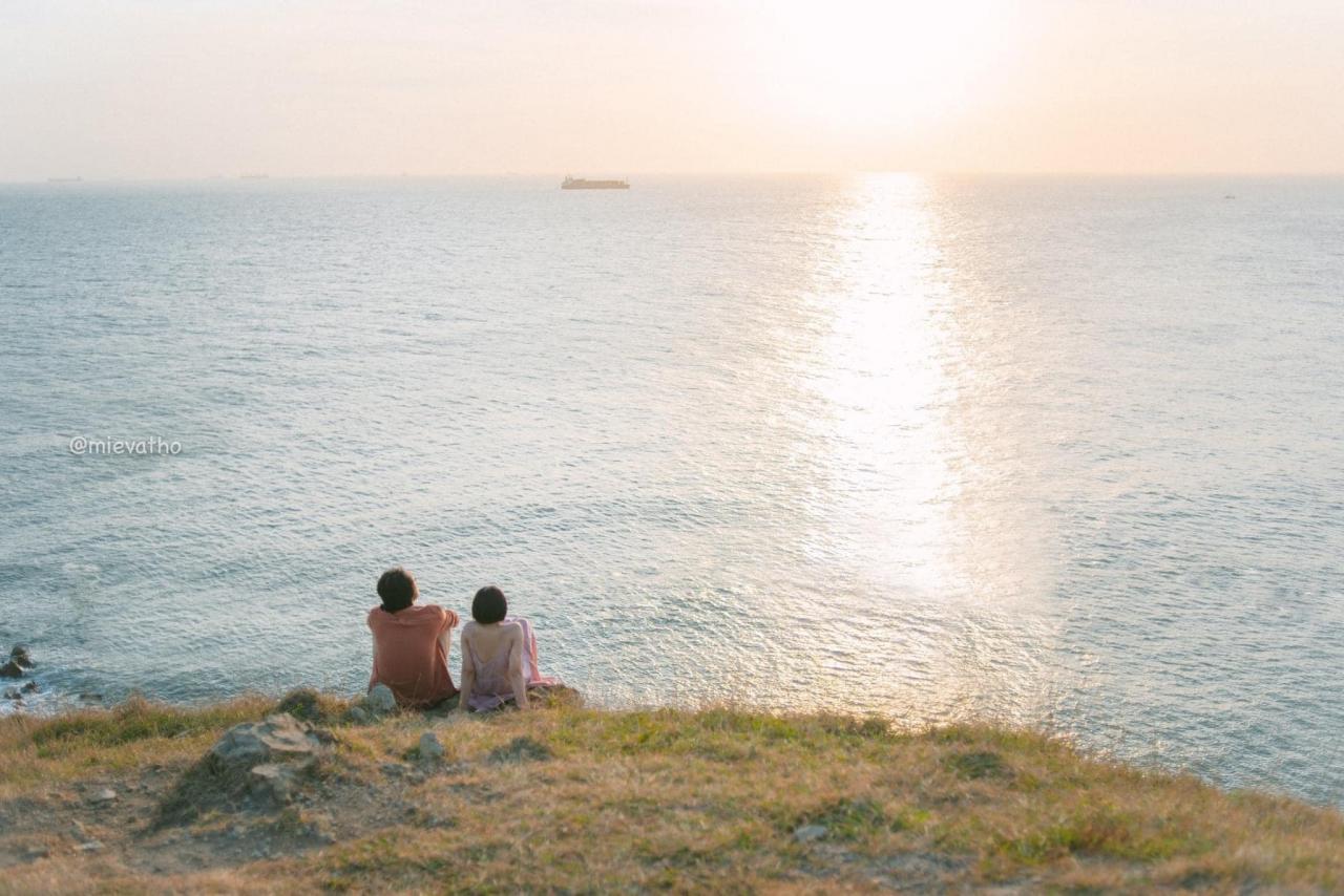 2 người đang ngồi trên nền đất nhìn về phía biển