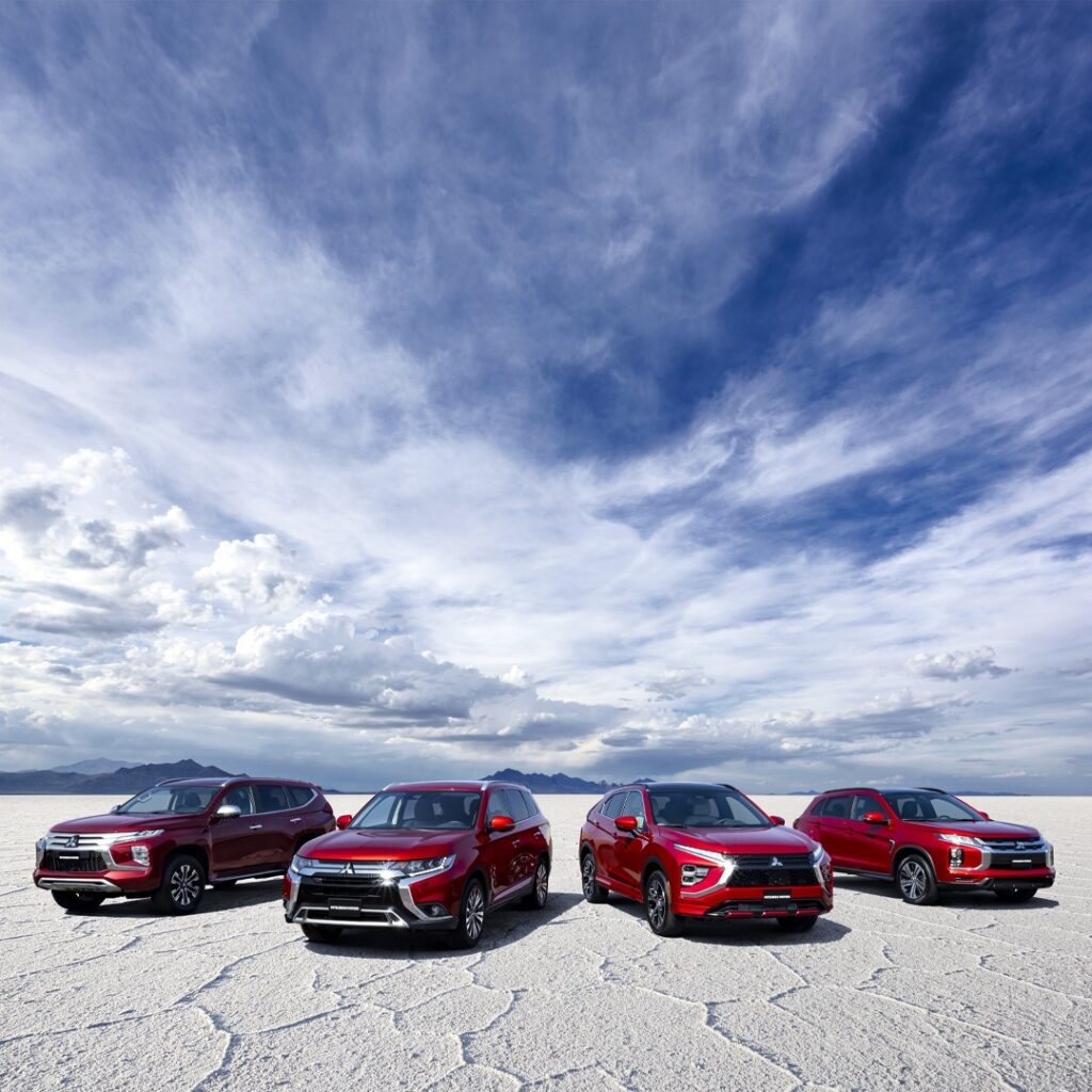 Có 4 chiếc xe màu đỏ đứng trên nền cát màu trắng, phía sau là bầu trời xanh nhiều mấu trắng