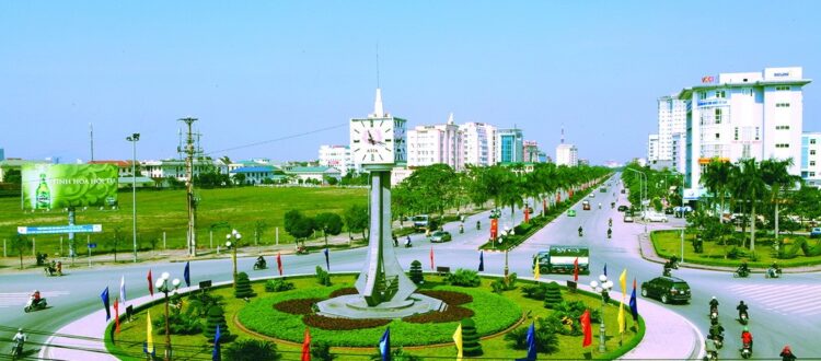 khuôn viên có vườn cỏ và các lá cờ màu vàng, xanh, đỏ và một cây đồng hồ lớn ở giữa xa xa là các toà nhà cao tầng ,tại thuê xe oto tại Nghệ An 